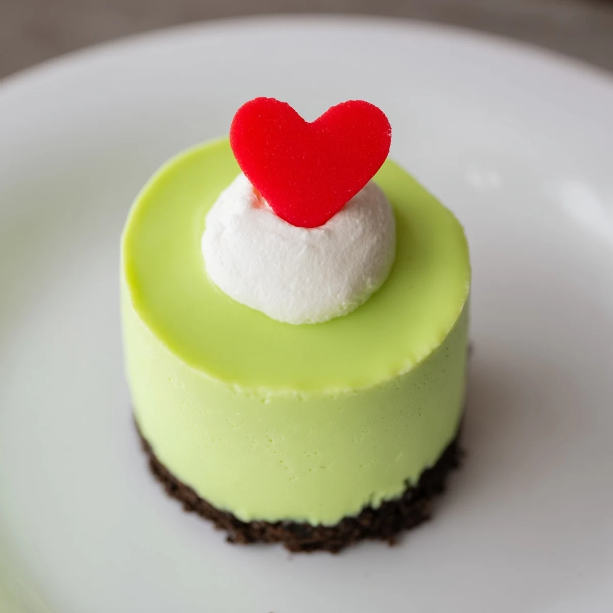 Festive Grinch Mini Cheesecakes, bright neon green, topped with whipped cream and joyful red heart sprinkles.
