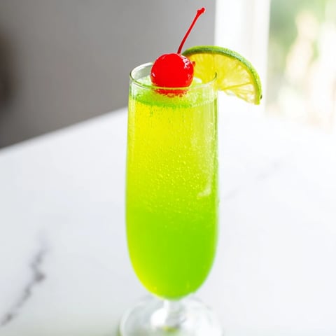 Bright green Quick Grinch Mimosa Mocktails, garnished with cherries, offer a refreshing holiday sip.