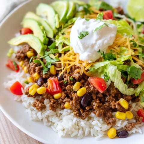 A colorful loaded beef burrito bowl, brimming with layers like cheese, sour cream, and cilantro.