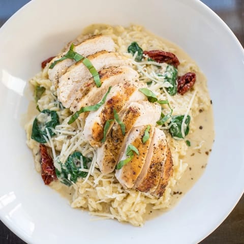 A close-up of Marry Me Chicken Orzo, with creamy sauce and golden chicken slices, garnished beautifully.