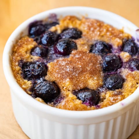 Warm, comforting Blueberry Baked Oats, pictured with a drizzle of maple syrup and a scoop of yogurt.