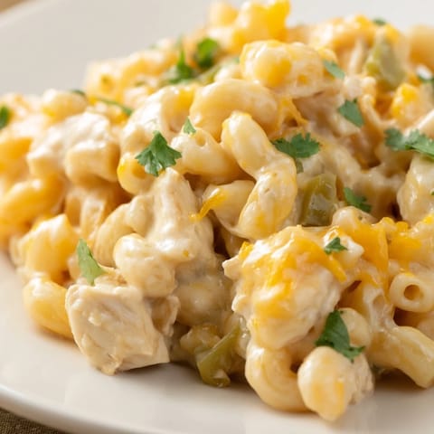 A steaming skillet of Green Chili Chicken Mac reveals creamy sauce clinging to tender elbow pasta, melted Monterey Jack, and green chiles flecked with fresh cilantro.  