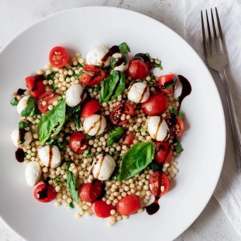 Tender Israeli couscous forms the base of this Caprese Couscous Salad, mingling with halved tomatoes, mozzarella balls, and torn basil leaves for a refreshing Mediterranean-inspired bite. 